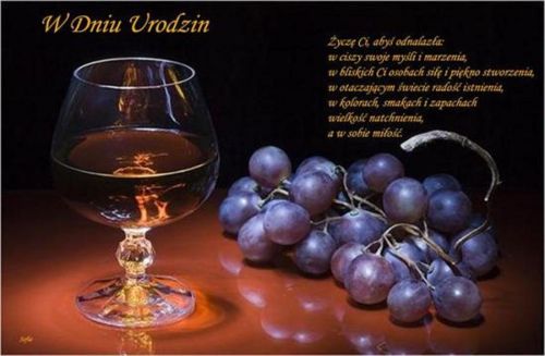 Kieliszek z koniakiem i ciemne winogrona na stole oraz życzenia urodzinowe i napis W Dniu Urodzin