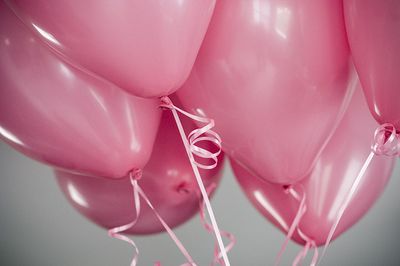 Zbiornik lśniących, różowych balonów w kształcie serc przewiązanych wstążkami na szarym tle