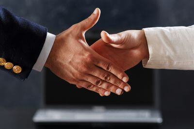 Biznesowy u�cisk d�oni dw�ch os�b na tle rozmytego laptopa w biurze