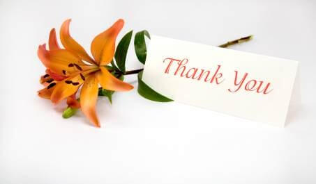 Pomarańczowa lilia z zieloną łodygą oraz biały bilecik z czerwonym napisem Thank You